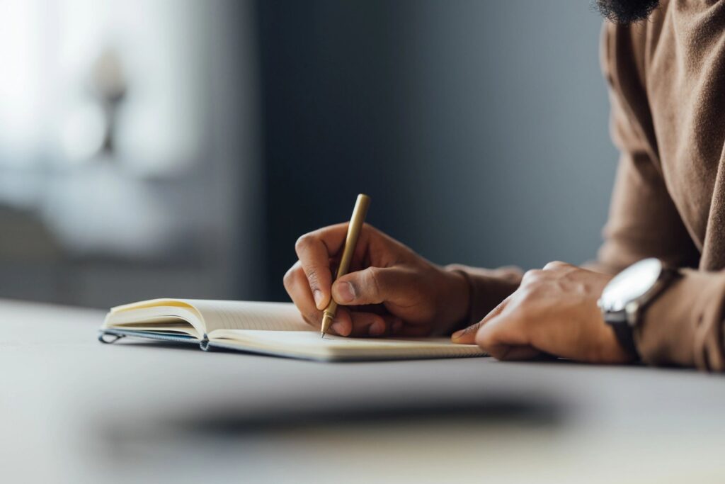 Close-up of Man Writing in a Notebook at a Desk