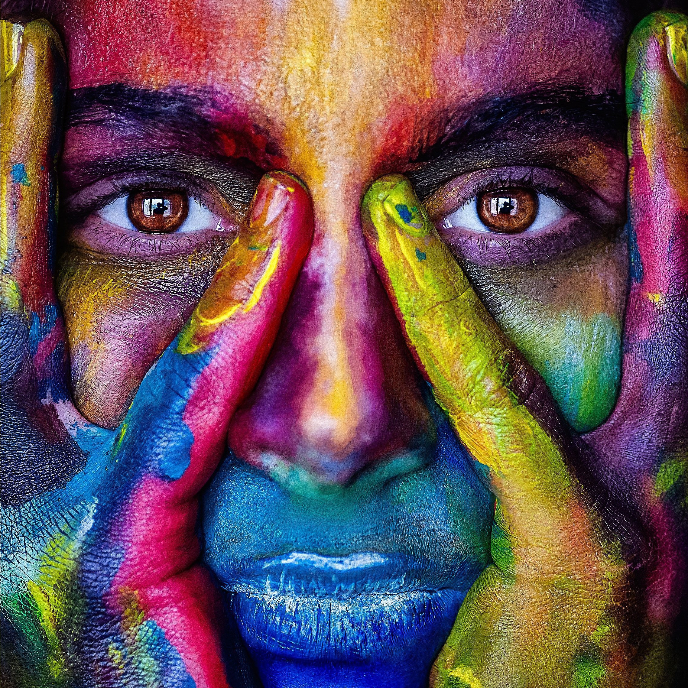 Woman with face and hands covered in colorful paint.